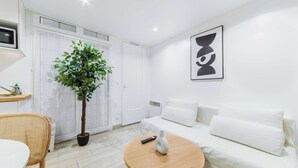 Un salon moderne avec un canapé blanc, une table basse ronde en bois, une plante en pot et une œuvre d’art abstraite accrochée au mur.