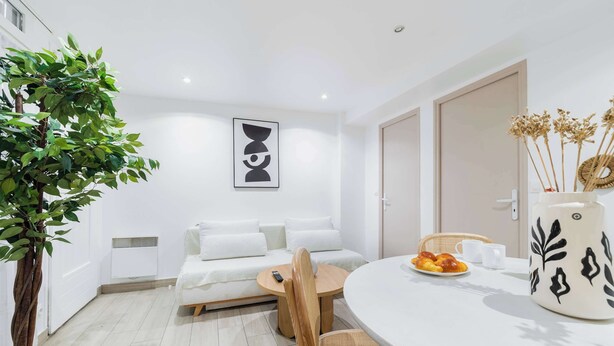 Une pièce moderne avec un canapé, une table à manger agrémentée d’un vase et une plante en pot.