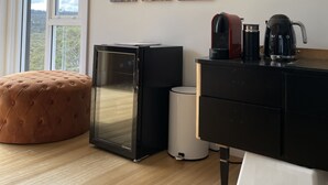 A modern living room with a large window, a black refrigerator, a coffee maker, and a framed family photo on the wall.