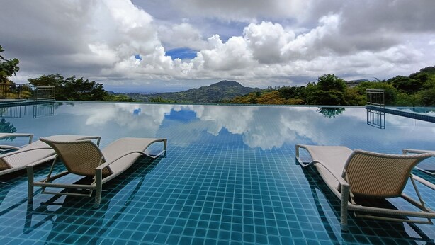 A swimming pool with clear blue tiles, two lounge chairs, and a mountainous landscape in the background. - Mist Mountain Resort powered by Cocotel (Cebu City)