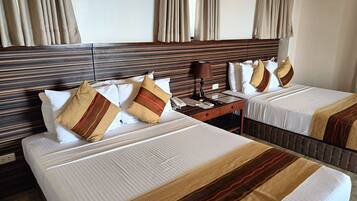 A hotel room with two beds, each with white linens and striped blankets. There is a wooden headboard, a nightstand with a lamp, and a window with curtains.