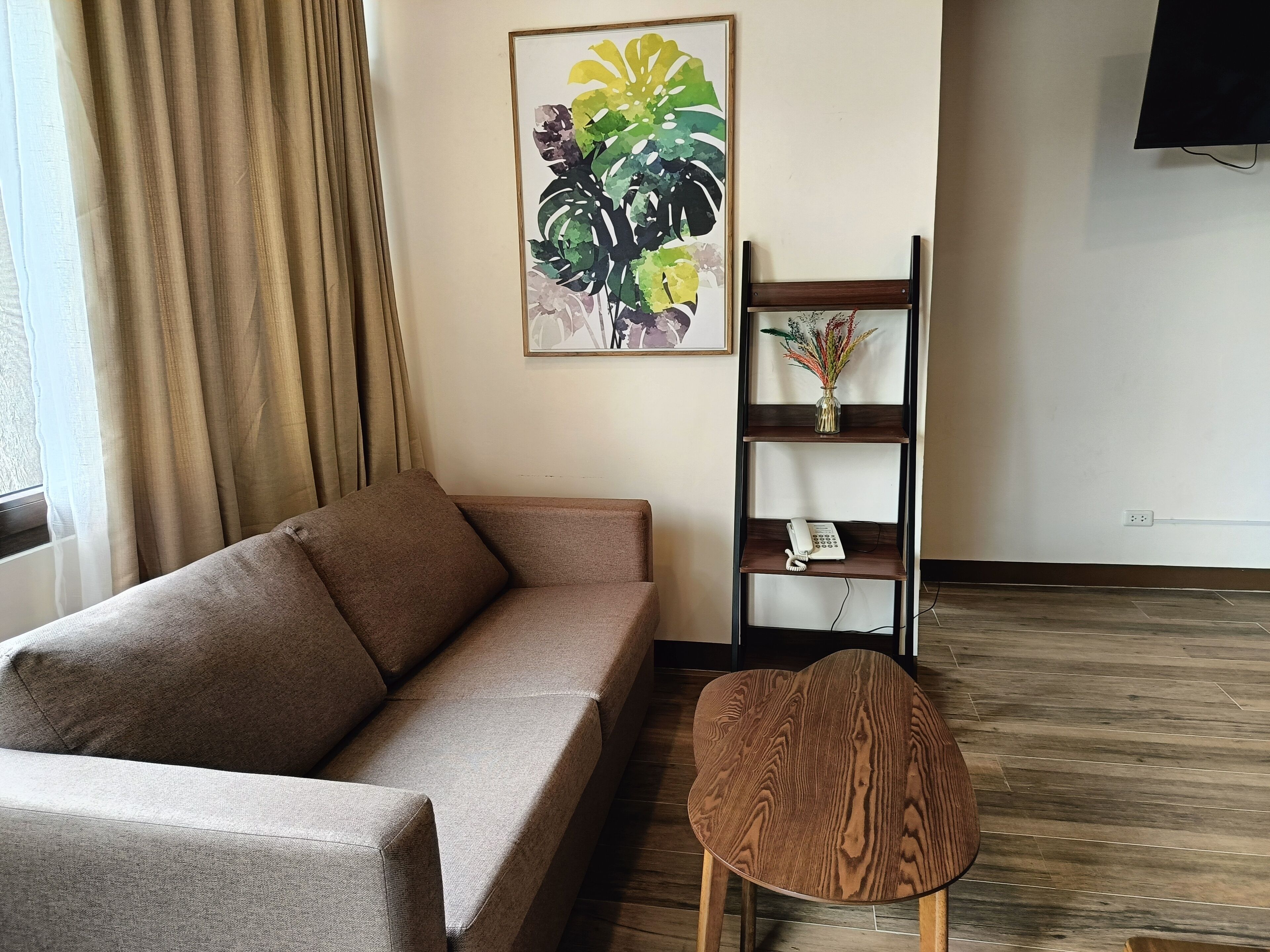 A living room with a sofa, a wooden chair, a bookshelf with a vase and a phone, and a painting on the wall.