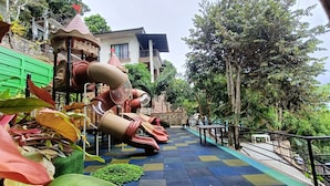 A playground with slides and climbing structures, surrounded by greenery and a building in the background. - Mist Mountain Resort powered by Cocotel (Cebu City)