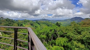 A scenic view from a balcony with a railing, overlooking a lush green landscape with hills and a partly cloudy sky. - Mist Mountain Resort powered by Cocotel (Cebu City)