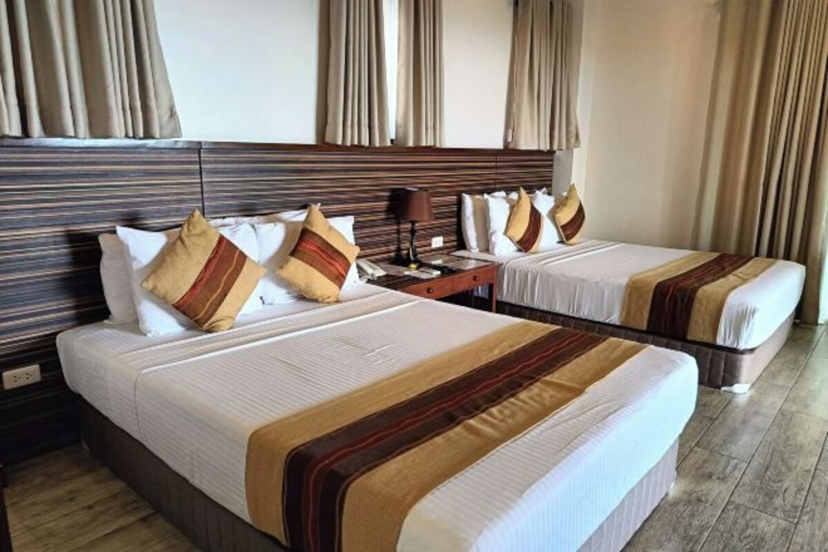 Habitación de hotel con dos camas, cada una con ropa de cama a rayas y almohadas a juego. Entre las camas hay una mesita de noche con una lámpara.
