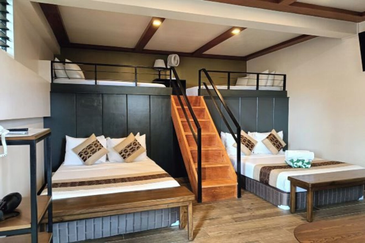 Habitación de hotel con dos camas, una escalera, un escritorio y una mesita de noche.