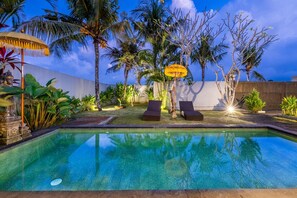 A swimming pool with two lounge chairs, surrounded by tropical plants and a wooden fence. - 888 Residence Villa with Private Pool (Ubud)