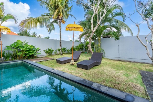 A pool area with lounge chairs and umbrellas, surrounded by palm trees and a white wall. - 888 Residence Villa with Private Pool (Ubud)
