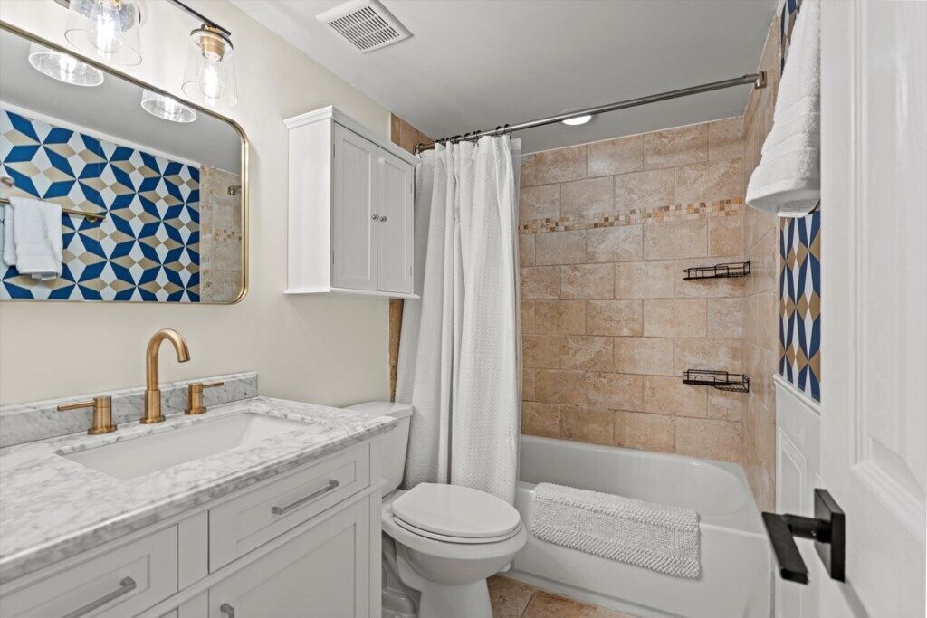 A bathroom with a marble sink, a white toilet, a shower with a beige tiled wall, and a white towel hanging on the wall.