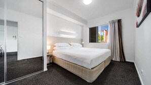 A modern hotel room with a large bed, a bedside table, a nightstand, a mirror, and a window with curtains.