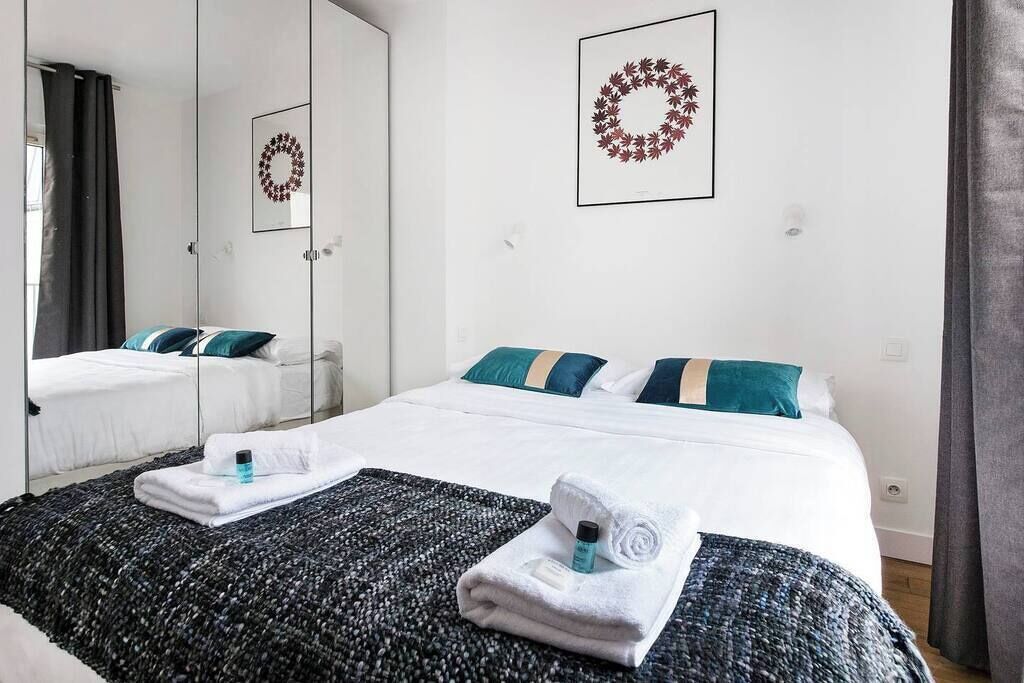 A hotel room with two beds, a large mirror, and a framed wreath on the wall.