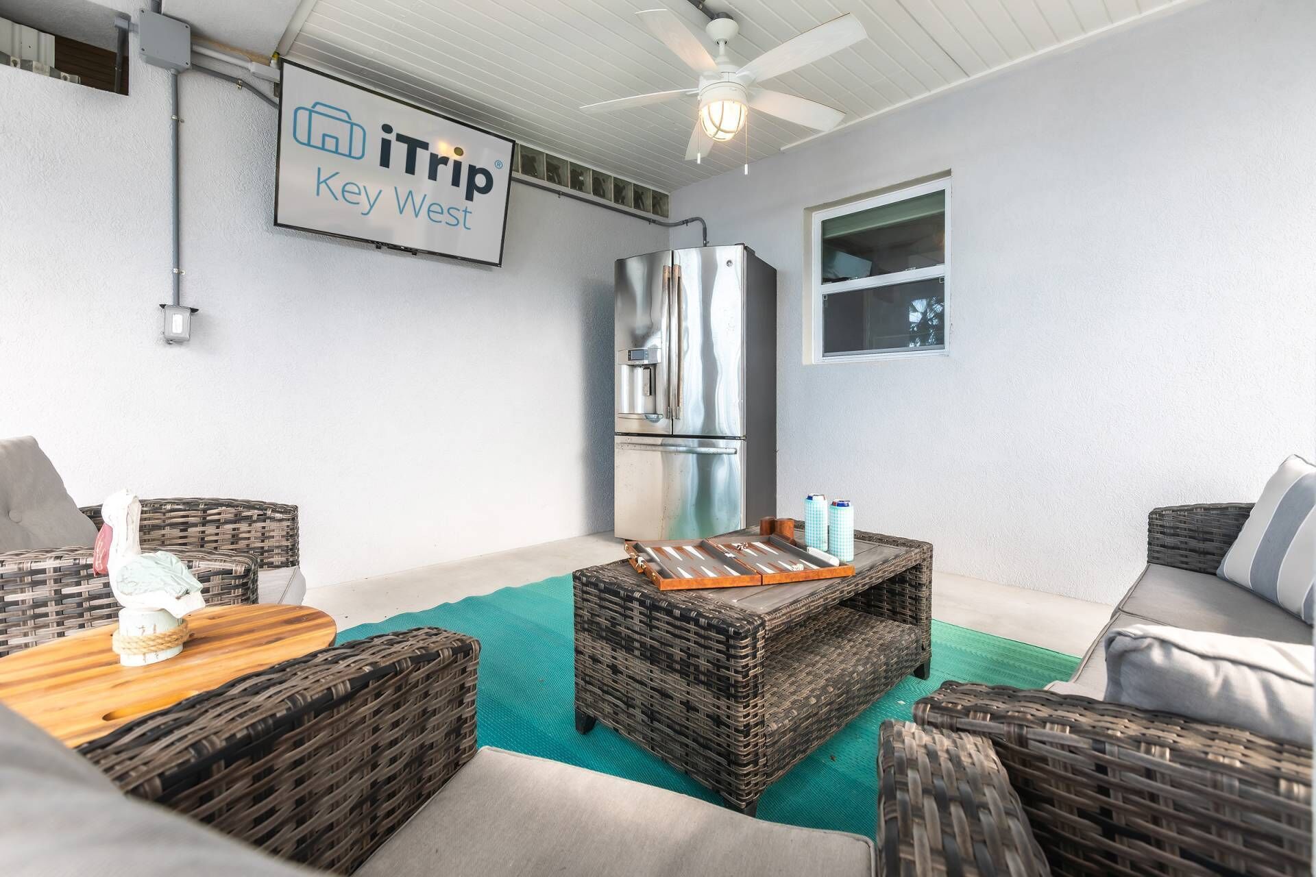 A modern outdoor living area with wicker furniture, a stainless steel refrigerator, and a ceiling fan.