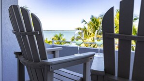 Un balcon agrémenté de fauteuils Adirondack et d’une table, offrant une vue sur une plage bordée de palmiers et sur l’océan.