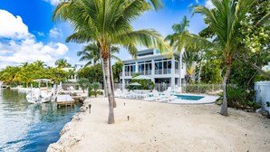 Une propriété située en bord de mer, dotée d’une piscine, de palmiers et de bateaux.