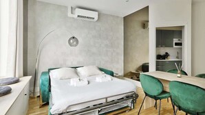 Una habitación de hotel moderna con cama, mesita de noche, lámpara y una pequeña cocina.