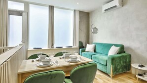 Una sala de estar moderna con un sofá verde, una mesa de comedor para cuatro personas y un ventanal con cortinas.