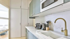 Una cocina moderna con armarios blancos, una campana extractora de acero inoxidable, un microondas integrado y un lavamanos con grifo dorado.