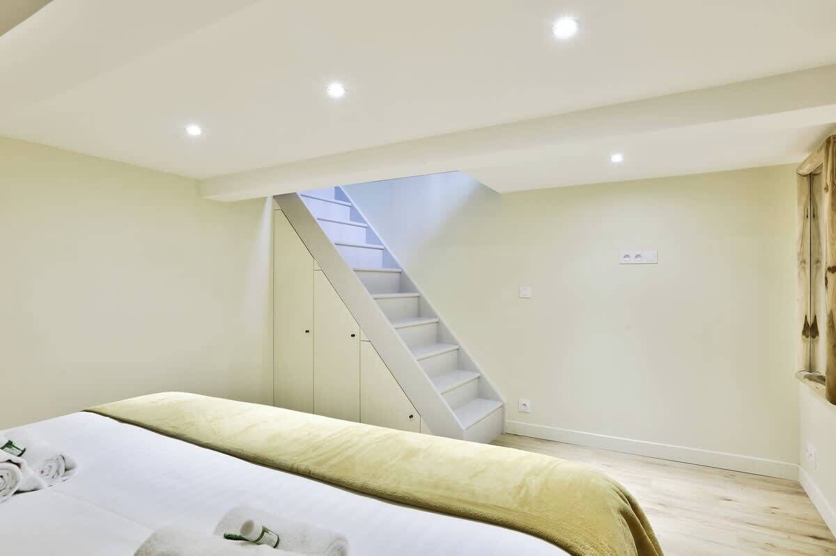A bedroom with a bed, a staircase, and a door.