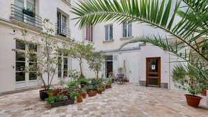 A courtyard with potted plants, a bicycle, and a building with multiple windows and doors.