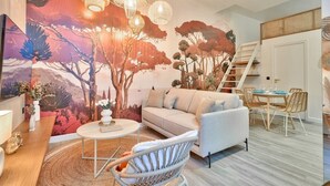 A living room with a sofa, a round coffee table, wicker chairs, a dining table with chairs, and a staircase.