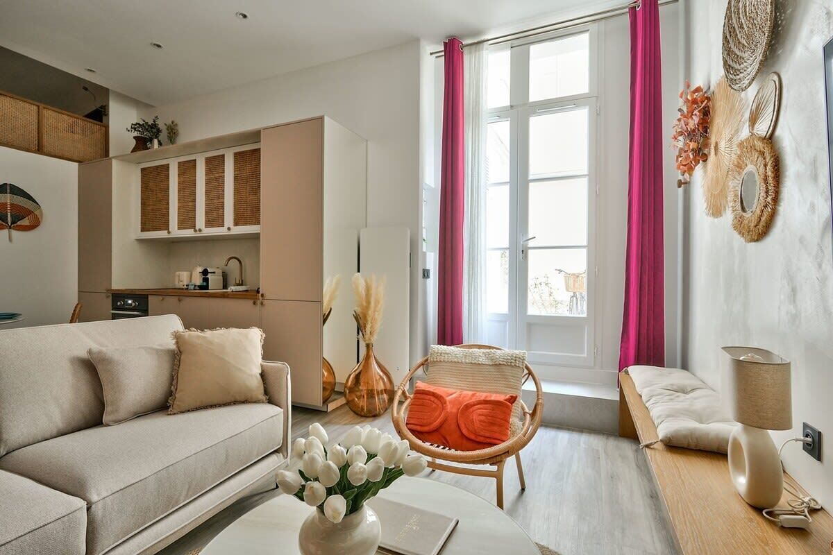 Ein modernes Wohnzimmer mit einer Couch, einem Korbsessel, einem Tisch mit Blumenvase und einem Fenster mit Vorhängen.