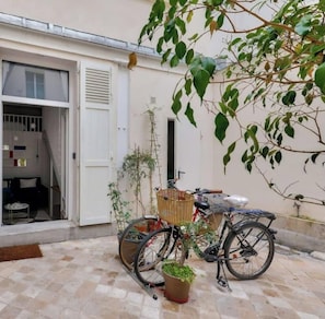 Un patio con una bicicleta, una planta en maceta y una cesta.