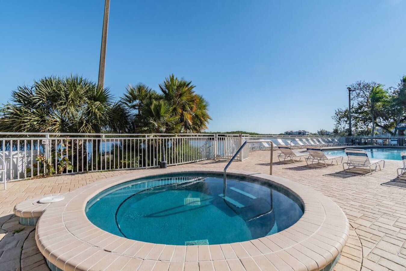 Un jacuzzi circulaire avec une piscine, entouré de chaises longues et de palmiers.