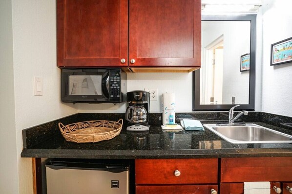 A kitchen with a microwave, coffee maker, sink, and a basket on the counter.