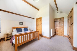 Un dormitorio con una cama de madera, una mesita de noche, una lámpara fijada a la pared y una puerta que da a otra habitación.