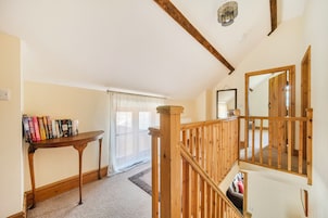 A staircase with wooden railings leading to an upper floor, a bookshelf with books, and a window with sheer curtains.