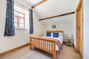 Un dormitorio con una cama de madera, una mesita de noche, una ventana con cortinas y una puerta de madera.