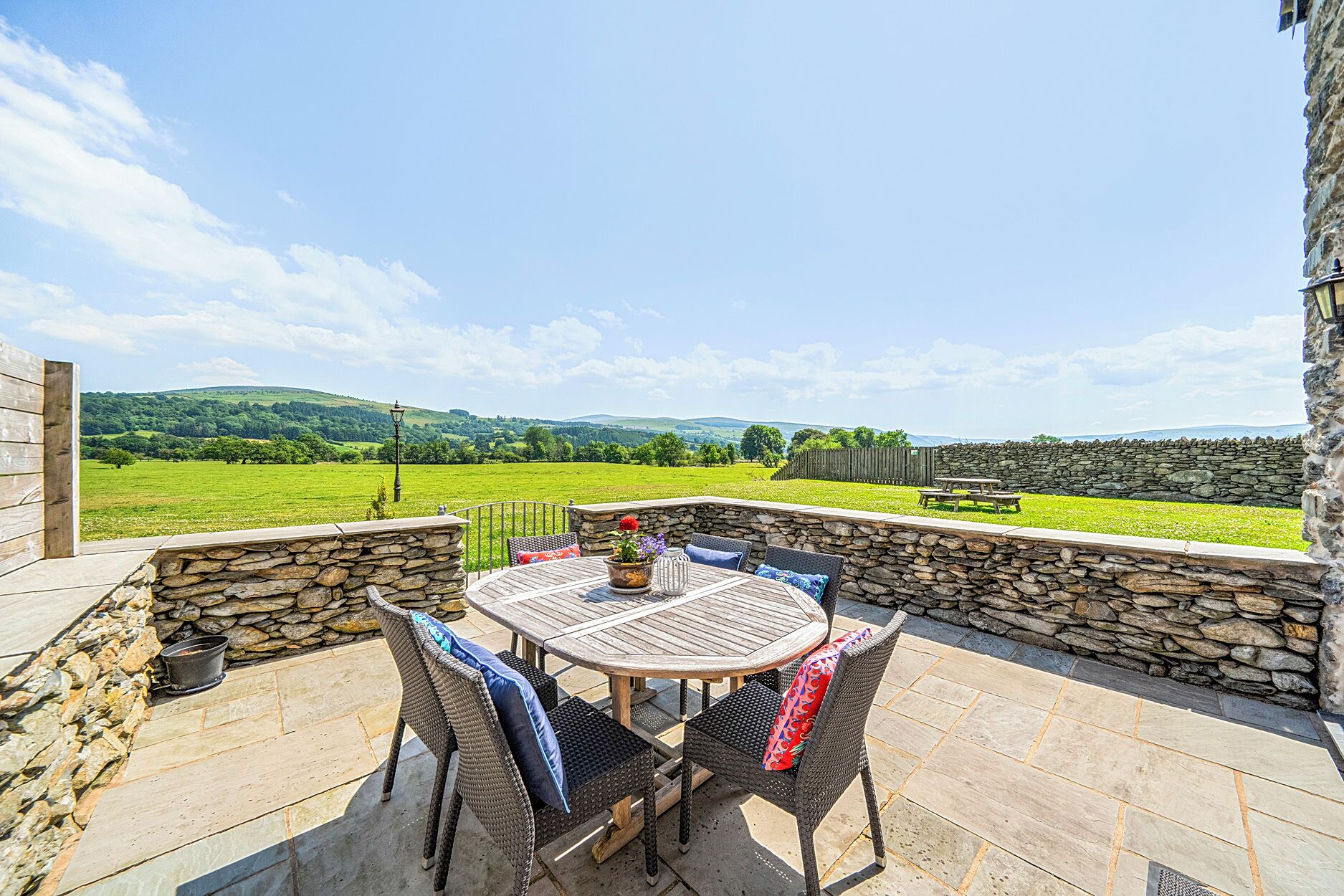 An outdoor patio with a stone wall, wicker chairs, and a table.