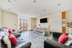 A spacious living area with a leather sofa, a wooden dining table, and a flat-screen TV mounted on the wall.
