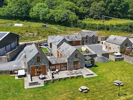 A cluster of stone buildings with a central patio area, surrounded by a grassy field and trees.