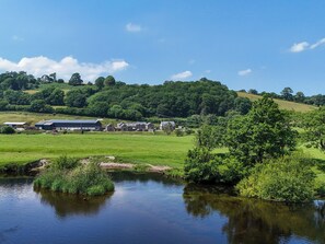 A rural landscape with a river, green fields, and a cluster of buildings including a large barn.