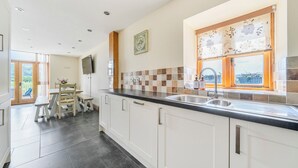 A modern kitchen with a large island, a built-in sink, and a window with a view. - Hay Store (Corwen)