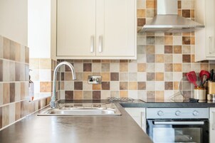 Una cocina con un lavamanos de acero inoxidable, estufa y salpicadero de azulejos.