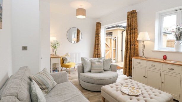 A modern living room with a sofa, armchair, ottoman, and a dining area with a table and chairs. - The Hollies (Norwich)