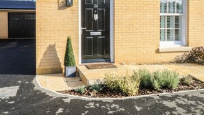 A residential building with a black front door marked with the number 23, a small potted plant, and a window with shutters. - The Hollies (Norwich)