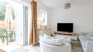 A modern living room with a sofa, a TV, and a dining area with chairs and an umbrella. - The Hollies (Norwich)