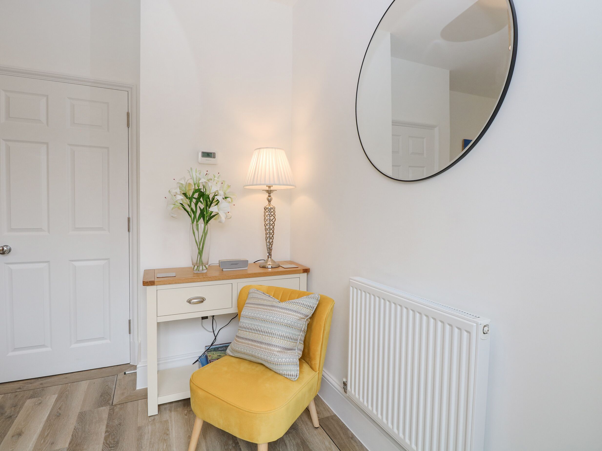 A room with a white door, a wooden desk with a lamp, a mirror, and a yellow chair.
