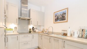 A modern kitchen with white cabinets, a stainless steel range hood, and a wooden floor. - The Hollies (Norwich)