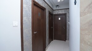 Un pasillo con dos puertas de madera, cada una con un número. Las paredes tienen una textura marcada y el suelo está cubierto de baldosas.