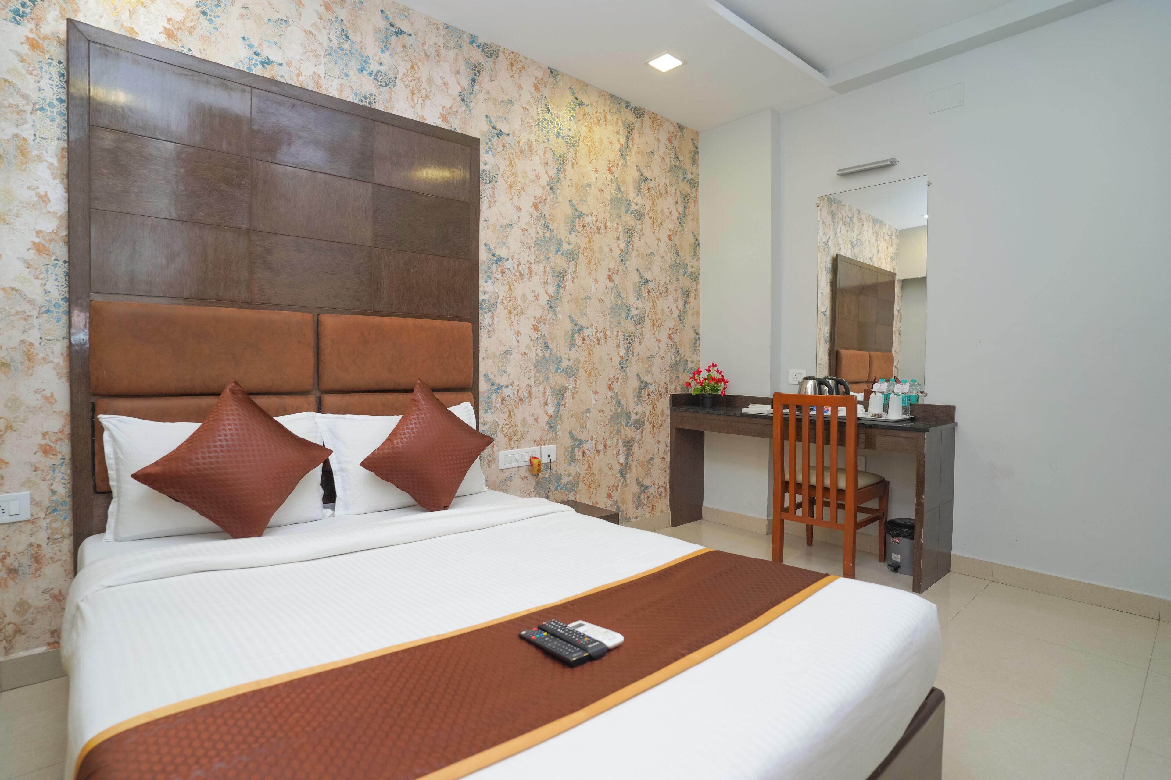 Quarto de hotel com cama grande, cabeceira de madeira, escrivaninha com cadeira e um espelho.