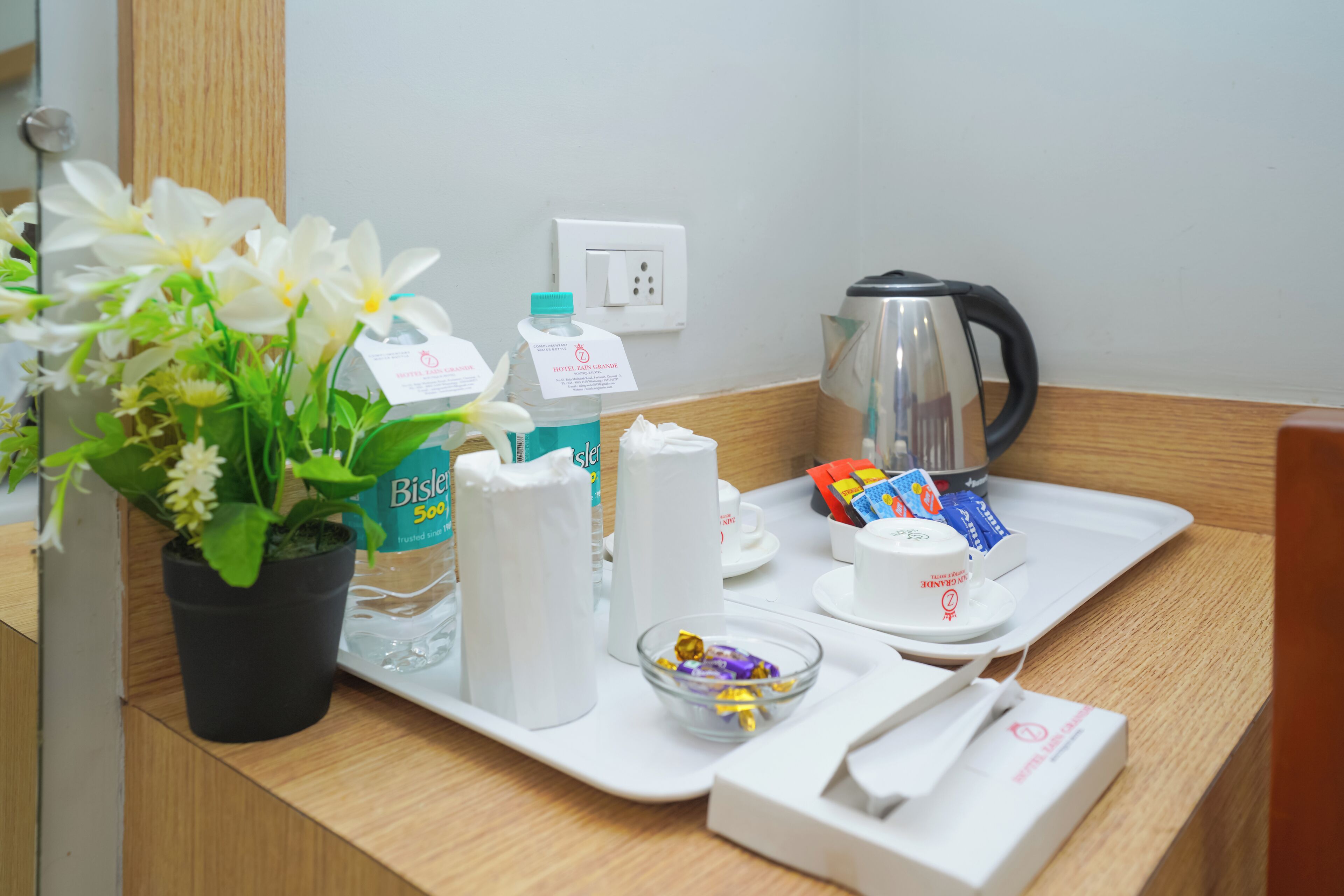 A hotel room's breakfast tray with a plant, Bisleri water bottles, a kettle, and tea packets.