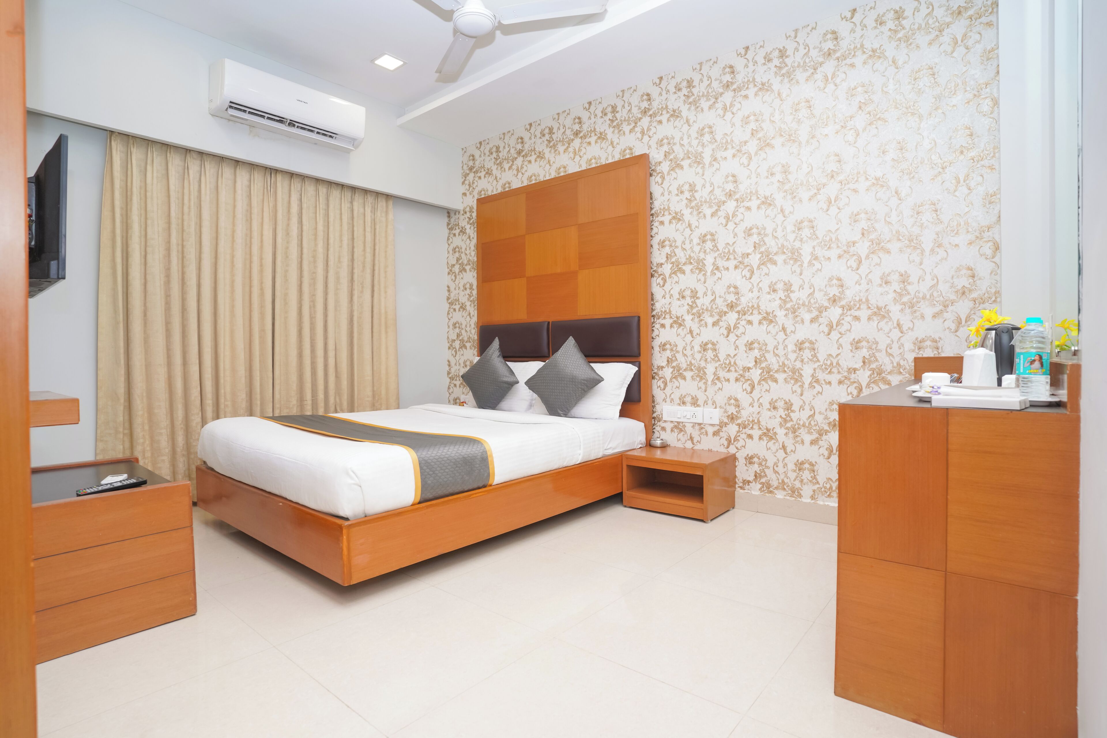 A modern hotel room with a wooden bed, a nightstand, a desk, and a wardrobe.