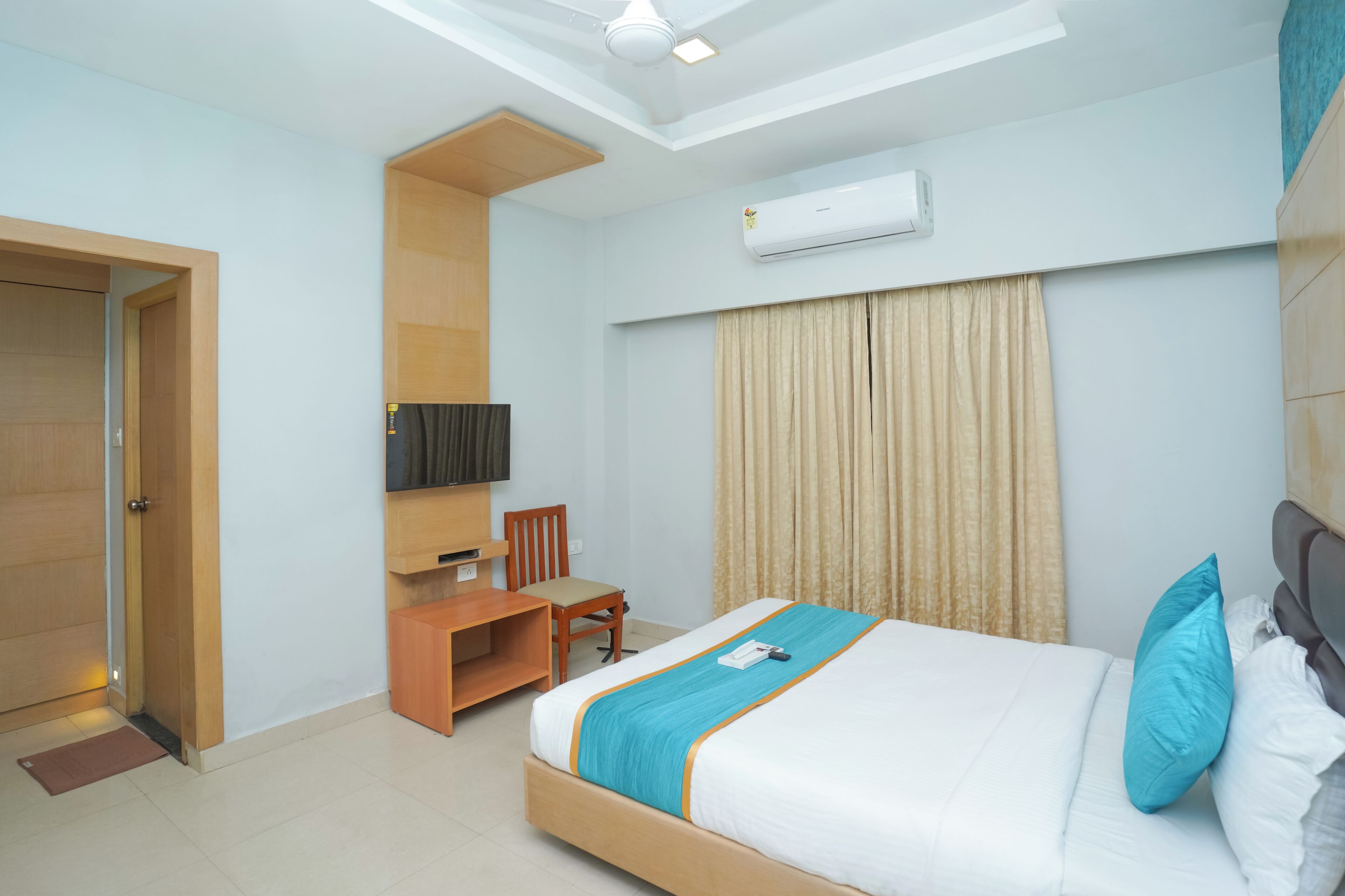 Quarto de hotel com cama, escrivaninha, cadeira, televisão e ar condicionado.