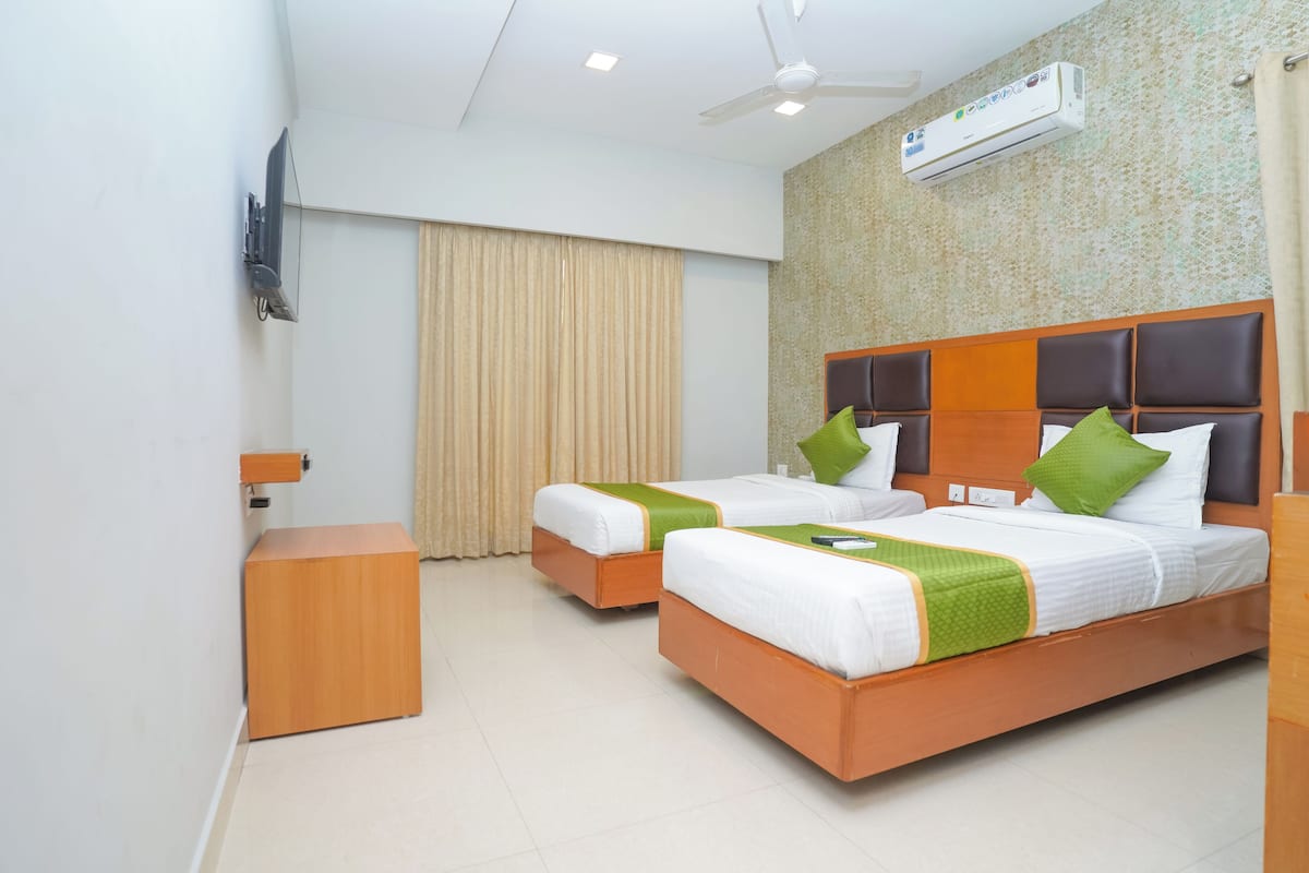 A hotel room with two beds, a wooden nightstand, a TV, and an air conditioning unit.