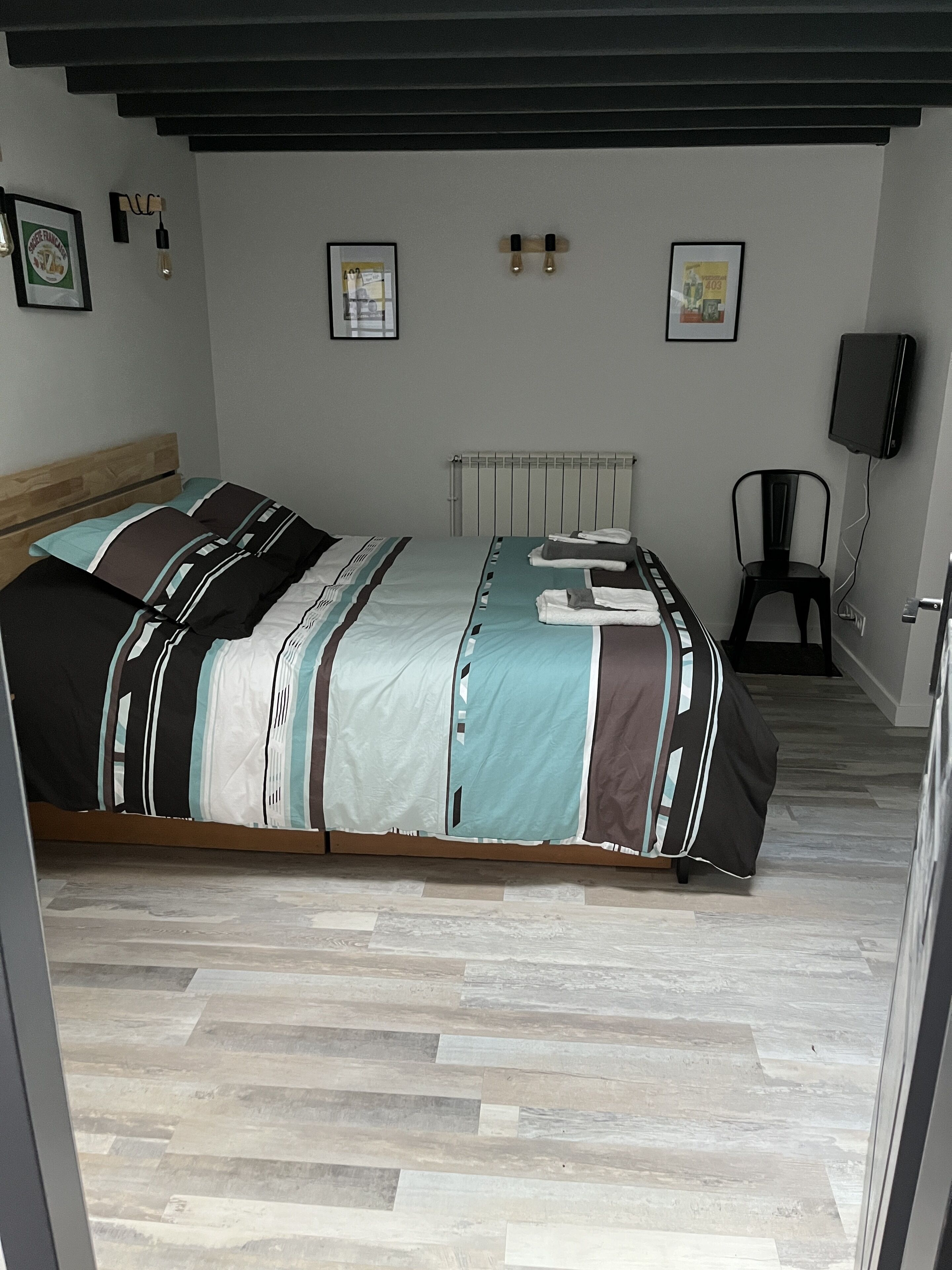 A bedroom with a bed, a radiator, a chair, and a television mounted on the wall.