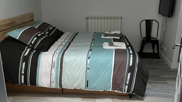 A bedroom with a bed, a radiator, a chair, and a television mounted on the wall.